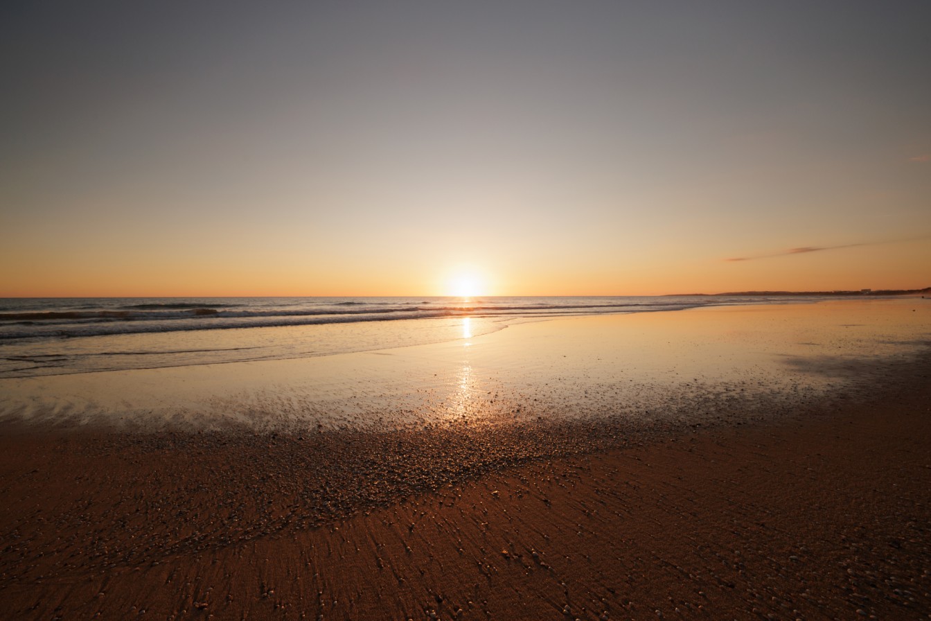 Serene sunset over a calm beach in Vilamoura, Algarve, with golden hues reflecting on the water.