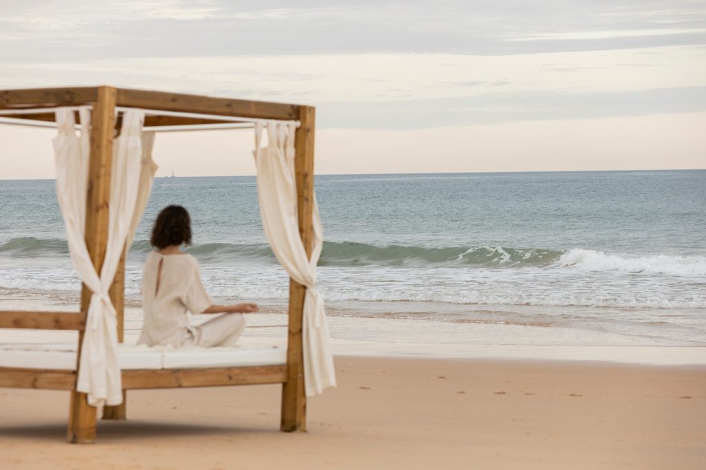 Person sitting on a beach cabana facing the ocean at dusk, Vilamoura Beach, Algarve.